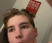 a young man stands in front of a sign that reads home run strike batter up