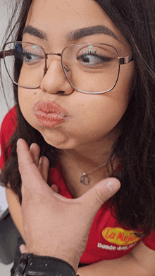 a woman wearing glasses and a red shirt that says la mejor makes a funny face