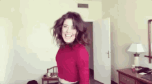 a woman in a red sweater is dancing in a room with the words hi written on the wall behind her .