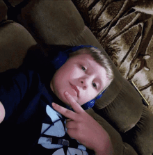 a young boy wearing headphones is laying on a couch and giving a peace sign