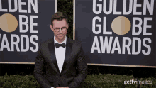 a man in a tuxedo and bow tie is standing in front of a sign that says golden globe awards