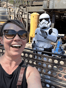 a woman wearing sunglasses smiles in front of a stormtrooper