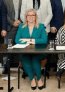 a woman in a teal suit is sitting at a table with a group of people behind her .