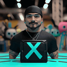 a man wearing a black shirt and a beanie holds a box with an x on it