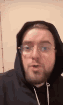 a man with a beard and glasses is wearing a hoodie and making a funny face .