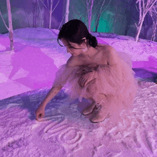 a woman in a tulle dress kneels in the snow and writes the word love on it