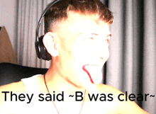 a man wearing headphones sticks out his tongue with the words they said b was clear behind him