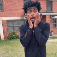 a man with his hands on his face looks surprised in front of a brick building