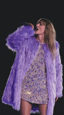 a woman singing into a microphone wearing a purple coat