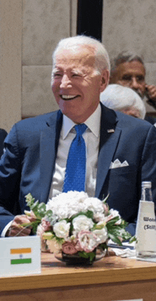 a man in a suit and tie is sitting at a table with flowers