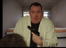 a man in a bathrobe is holding a gun in a bedroom