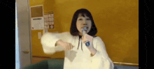 a woman in a white sweater is singing into a microphone in front of a yellow wall .