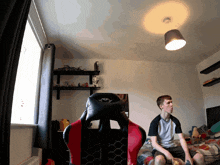 a man sits in a red and black gaming chair in a room