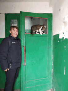 a boy standing next to a green door with a cat sitting on it