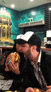 a man and a woman are eating a hamburger in front of a wall that says #share the burger love