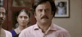 a man with a mustache is standing in front of a group of people and making a funny face .