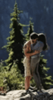 a man is holding a woman in his arms while they are hugging on top of a mountain .