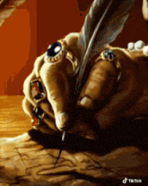 a painting of a hand holding a feather pen with the watermark tiktok on the bottom right