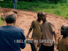 a group of men standing on a dirt road with the words " i believe in speed " written on the bottom