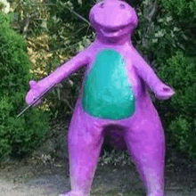 a statue of a purple dinosaur with a green belly is standing in front of trees .