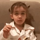 a little girl is sitting in a chair with her eyes closed and eating a cookie .