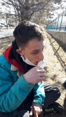 a young man wearing a mask and a blue jacket eating ice cream