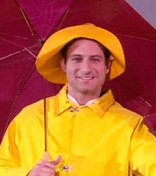 a man wearing a yellow raincoat and hat is holding a red umbrella .