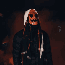 a man is wearing a pumpkin mask and a hood .