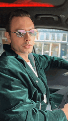 a man wearing sunglasses and a green jacket is sitting in a car