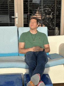 a man in a green polo shirt is sitting on a blue couch with his eyes closed