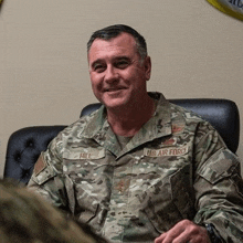 a man in a military uniform is sitting in a chair and smiling at the camera .