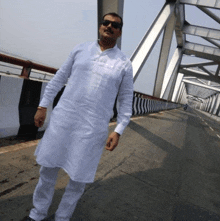 a man wearing sunglasses and a white shirt stands on a bridge