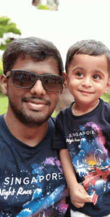 a man holding a little boy wearing a singapore night race t-shirt