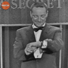 a man in a tuxedo is looking at his watch in front of a sign that says secret