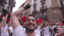 a man with a beard is standing in front of a crowd of people holding red scarves in their hands .