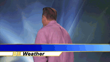 a man in a pink shirt is standing in front of a banner that says bbc weather