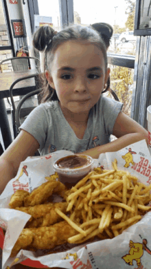 a little girl is sitting at a table with a plate of food that says ' chicken ' on it