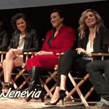 a group of women are sitting in director 's chairs in front of a screen . one woman is wearing a red dress .