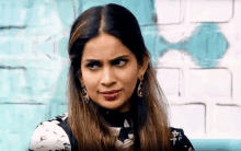 a woman wearing earrings is making a funny face in front of a blue brick wall .