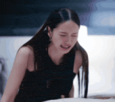 a woman in a black dress is crying while laying on a bed