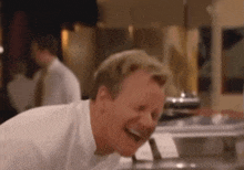 a man in a white shirt is laughing in a restaurant kitchen