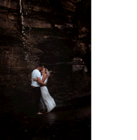 a man and woman are dancing in front of a waterfall and the woman is holding the man 's shirt