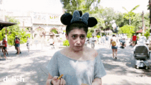 a woman wearing a minnie mouse ear headband is eating a snack in front of a building that says up