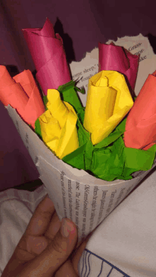 a person is holding a newspaper cone filled with flowers