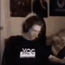 a man wearing headphones and a black shirt with the word xeg on it is standing in a room .