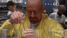 a man in a yellow jacket is pouring liquid into a glass with a straw