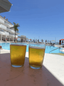 two glasses of beer are sitting on a table in front of a pool