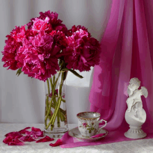 a vase of pink flowers next to a cup and saucer