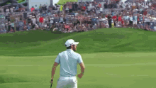 a man in a blue shirt and white hat is standing on a golf course with a crowd watching .