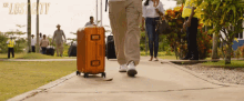 a man carrying an orange suitcase is walking down a sidewalk with the words " the lost city " written on the bottom